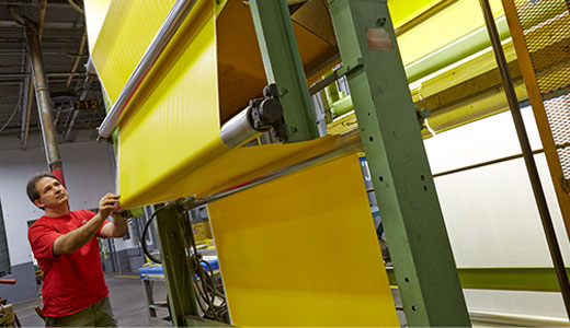 Man in red shirt operating a vinyl roller with yellow vinyl