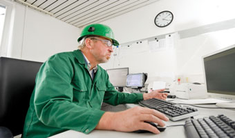 Man in green jumpsuit at a computer in a control room