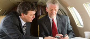 Two men in suits on a small jet looking at their phones