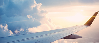 The wing of a aircraft mid-flight with the SAI Global AS9100 Certified System logo